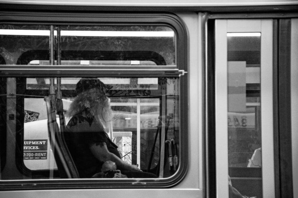 Black and white image of a bus interior featuring a bearded man reflecting in the window.