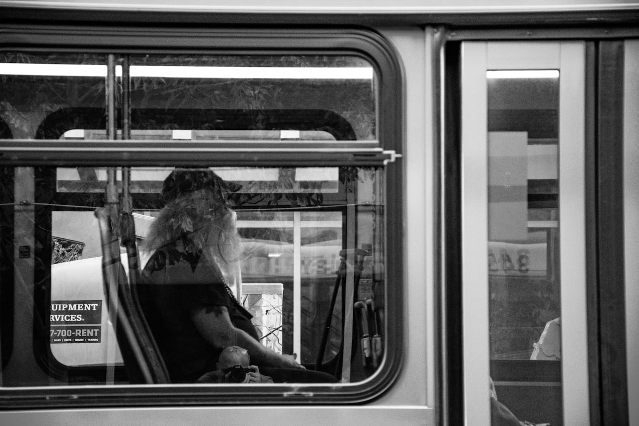 Black and white image of a bus interior featuring a bearded man reflecting in the window.
