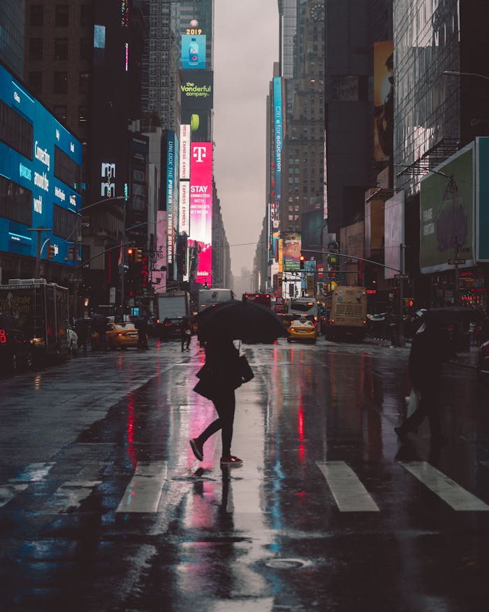 A person with an umbrella crossing Times Square at night, reflecting neon lights.