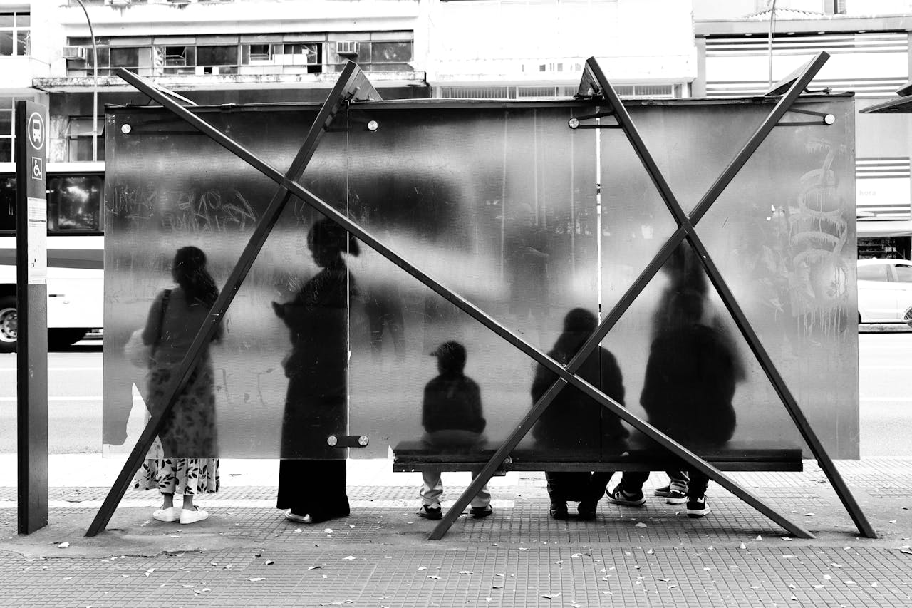 Black and white photo of people silhouetted at a bus stop, creating an urban abstract scene.